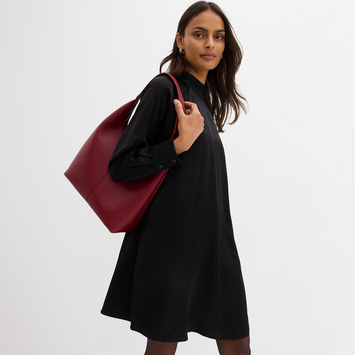 Schwarzes Kleid mit langen Ärmeln, kombiniert mit einer großen bordeauxroten Handtasche.