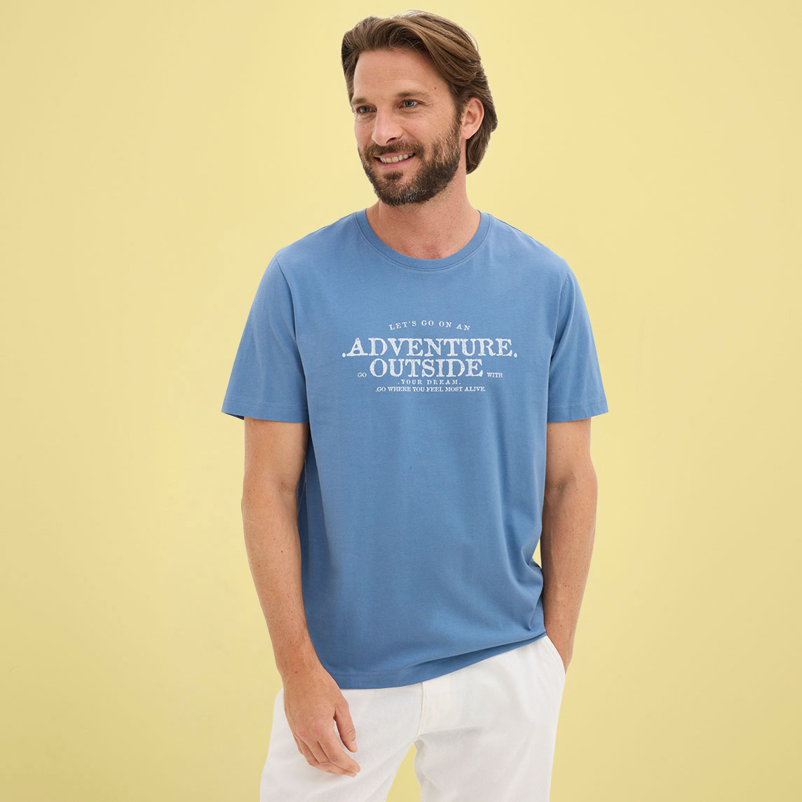 Mann trägt ein lässiges blaues T-Shirt mit weißem Aufdruck und helle Hose.