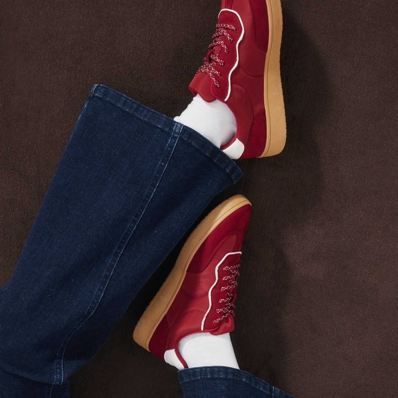 Rote Sneaker, weiße Socken und dunkelblaue Jeans bilden ein lässiges Outfit.