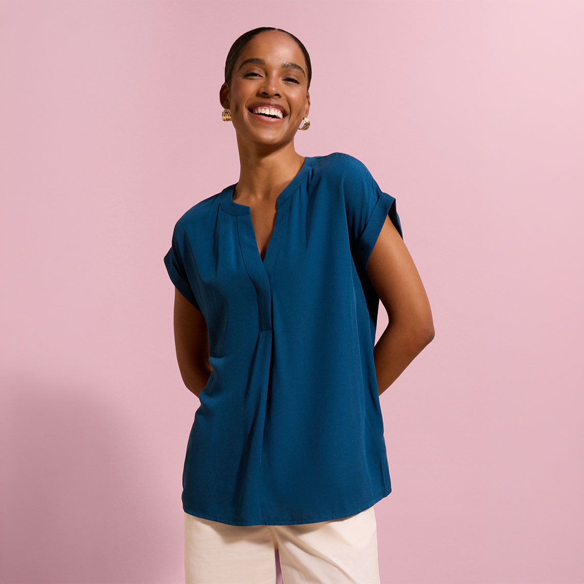 Modische tealfarbene Bluse mit V-Ausschnitt und hochgekrempelten Ärmeln, kombiniert mit heller Hose.