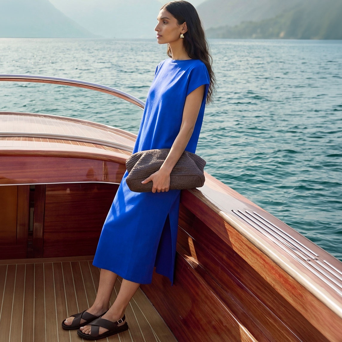Leuchtend blaues Midikleid, bequeme Sandalen und eine schicke texturierte Tasche.