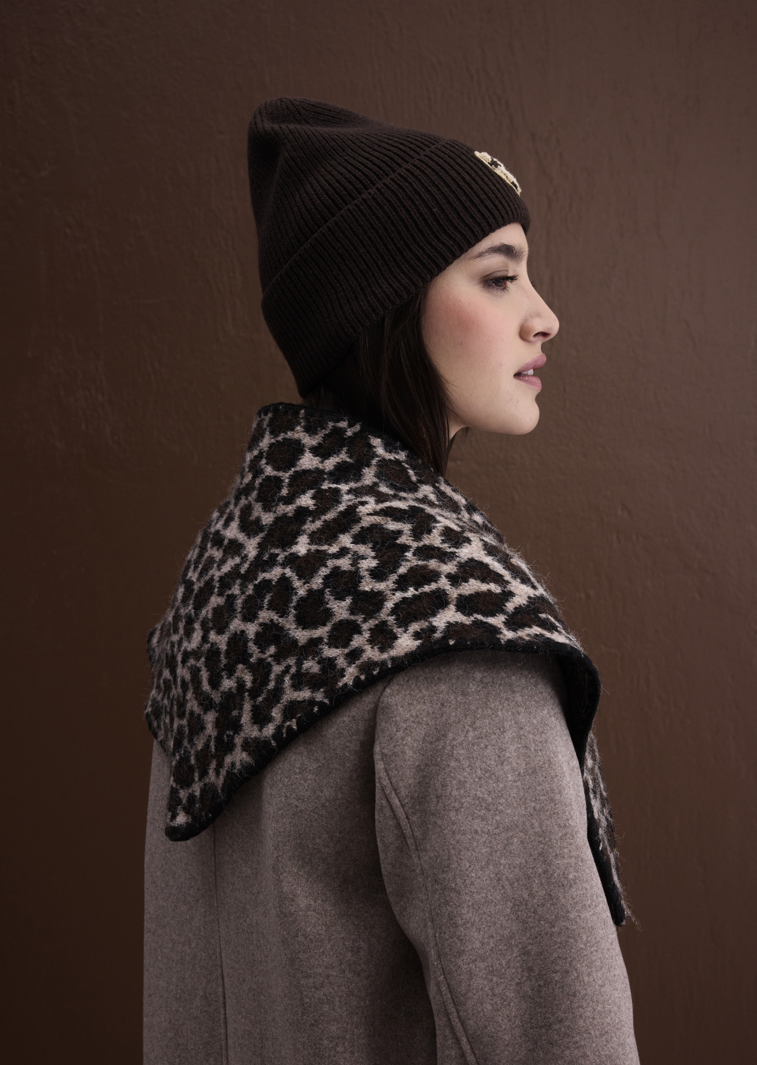 Modisches Winteroutfit: Dunkle Strickmütze, auffälliger Leoparden-Schal und warmer grauer Wollmantel.