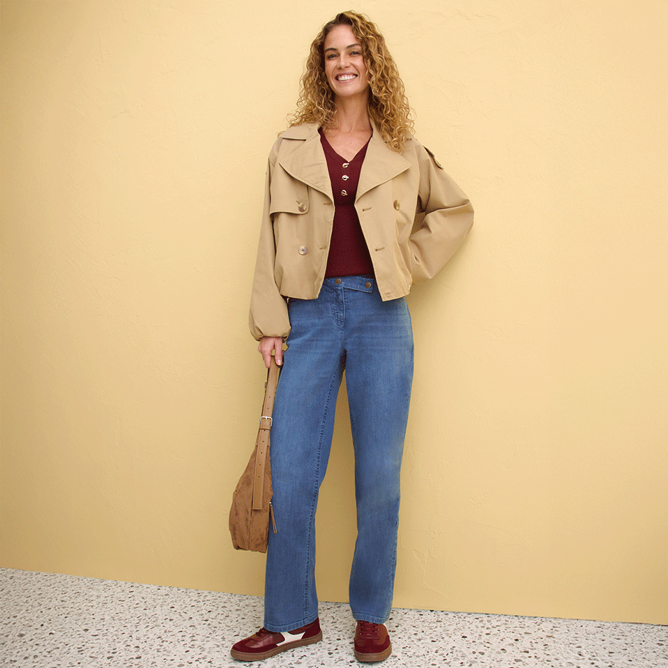 Beiger Trenchcoat über rotem Top, weite Jeans und braune Schuhe.