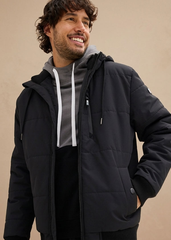 Der Mann trägt eine schwarze Steppjacke über einem grauen Kapuzenpullover.