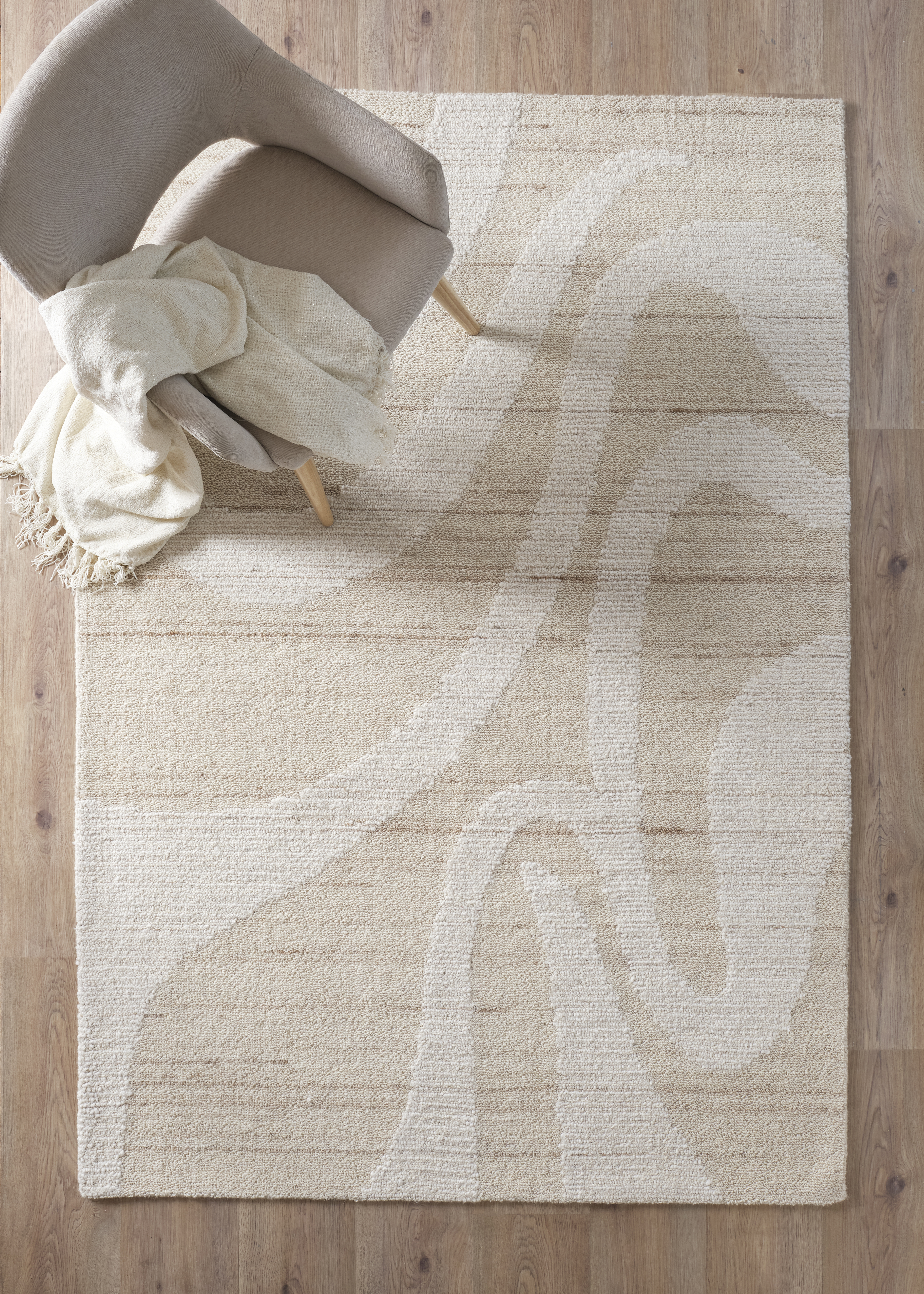 Eleganter cremefarbener Teppich mit subtilen Mustern, darauf ein gemütlicher Sessel und eine weiche Decke.