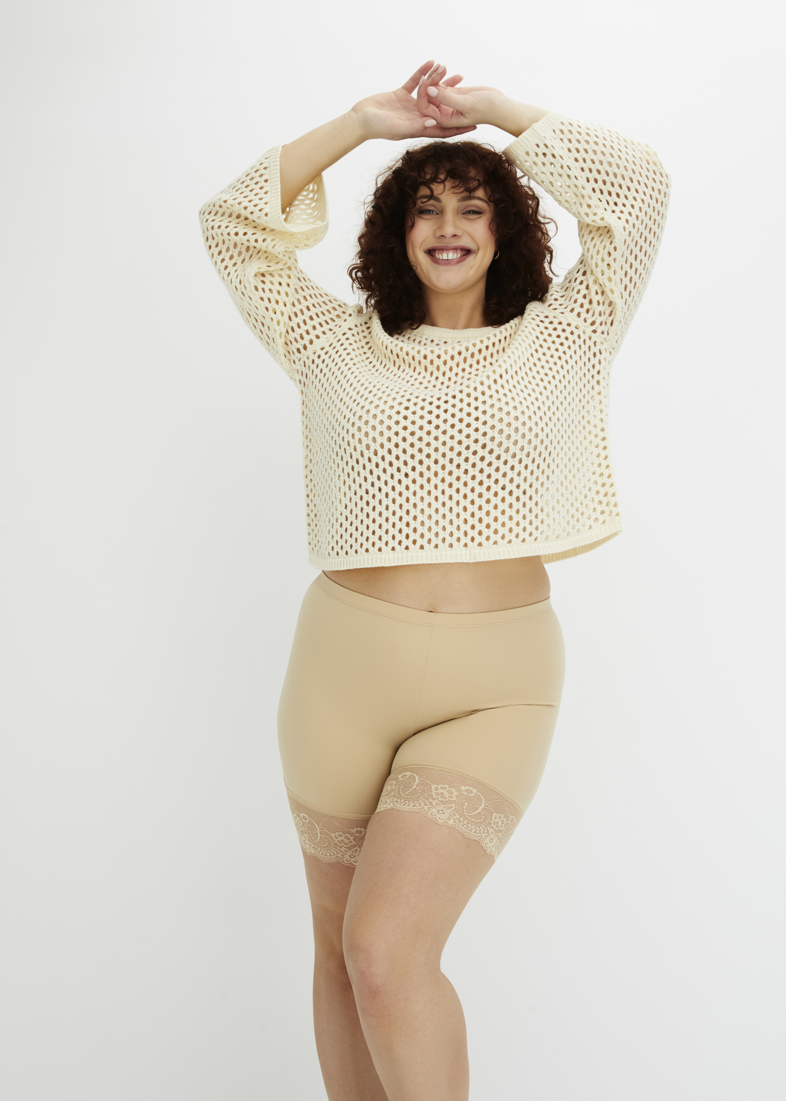 Die Frau trägt einen hautfarbenen Netzpullover und Shapewear-Shorts mit Spitzenbesatz.