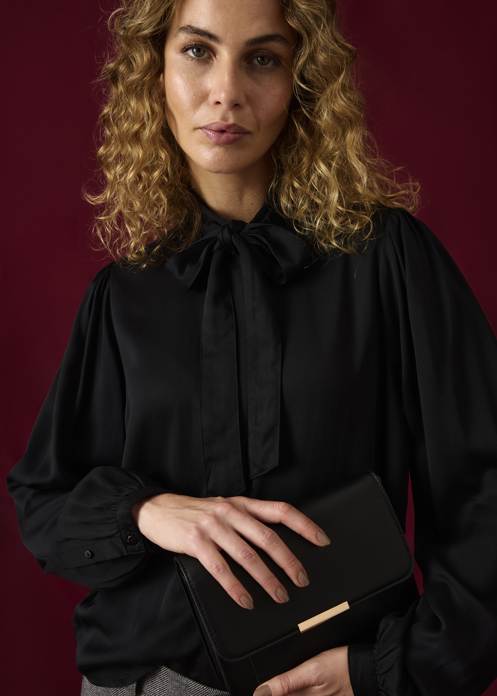 Schwarze Bluse mit eleganter Schleife und weiten Ärmeln, dazu eine schicke Clutch.