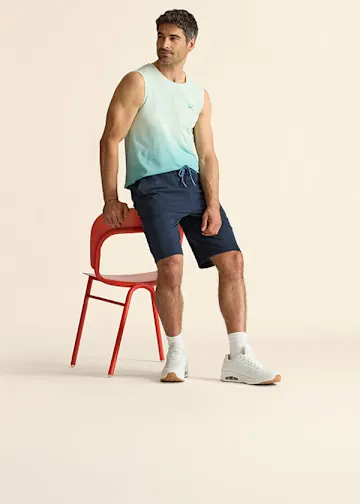 Trendiges ärmelloses Shirt mit Farbverlauf, dazu blaue Shorts und weiße Sneaker.