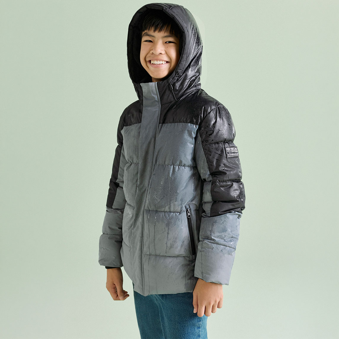 Das Kind trägt eine modische zweifarbige Steppjacke in Grau und Schwarz, dazu Jeans.