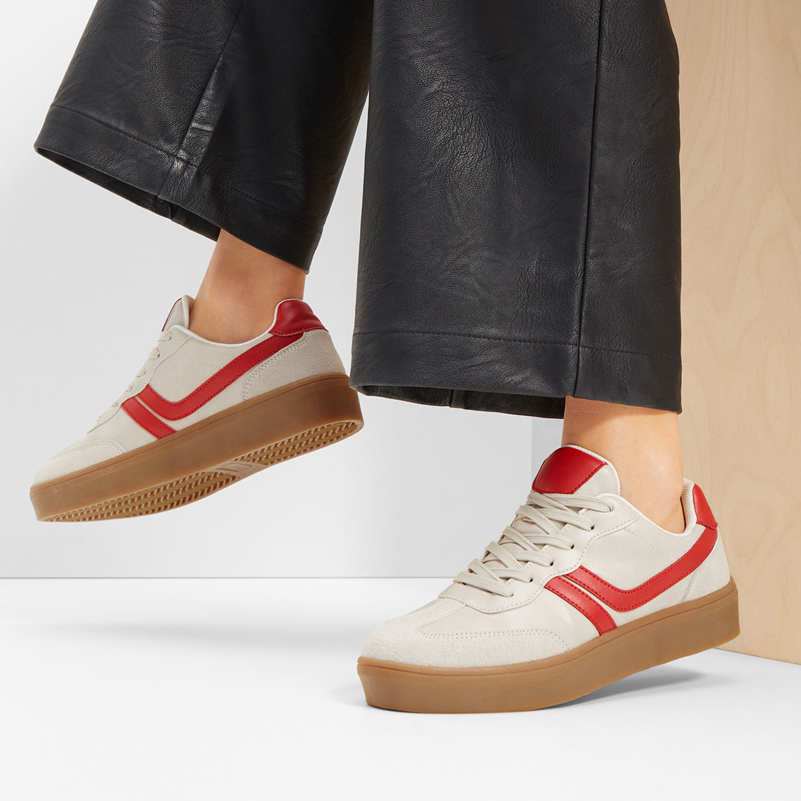 Weite schwarze Lederhose trifft auf lässige Sneaker mit rotem Akzent.