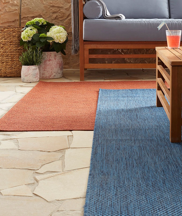 Lebendige Teppiche in Terrakotta und Blau schmücken den Boden vor einem grauen Sofa.