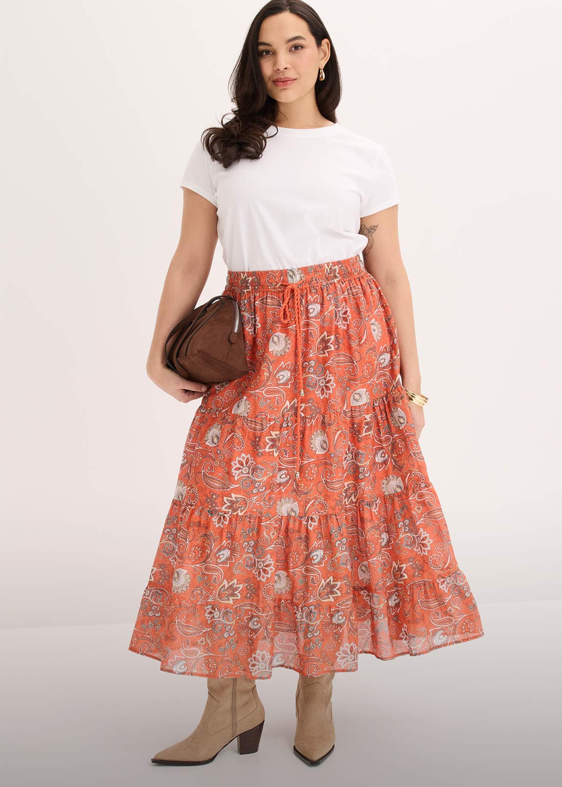 Weißes T-Shirt kombiniert mit orangefarbenem, gemustertem Maxirock. 