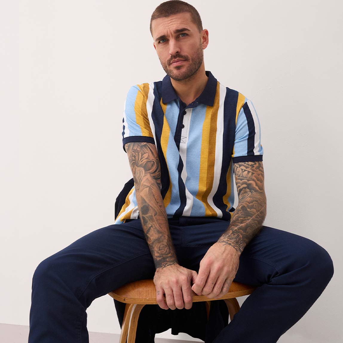 Gestreiftes Poloshirt in Blau, Gelb und Weiß. Dunkelblaue Hose. 