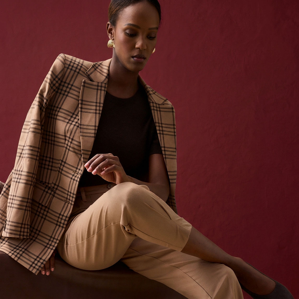 Karierter Blazer, dunkles Oberteil und beige Hose bilden ein elegantes Outfit.