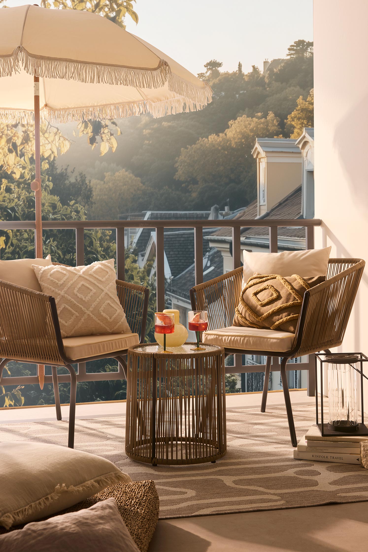 Gemütliche Terrasse mit Rattanstühlen und Sonnenschirm. Stilvolle Kissen in Erdtönen schmücken die Sitzgelegenheiten.