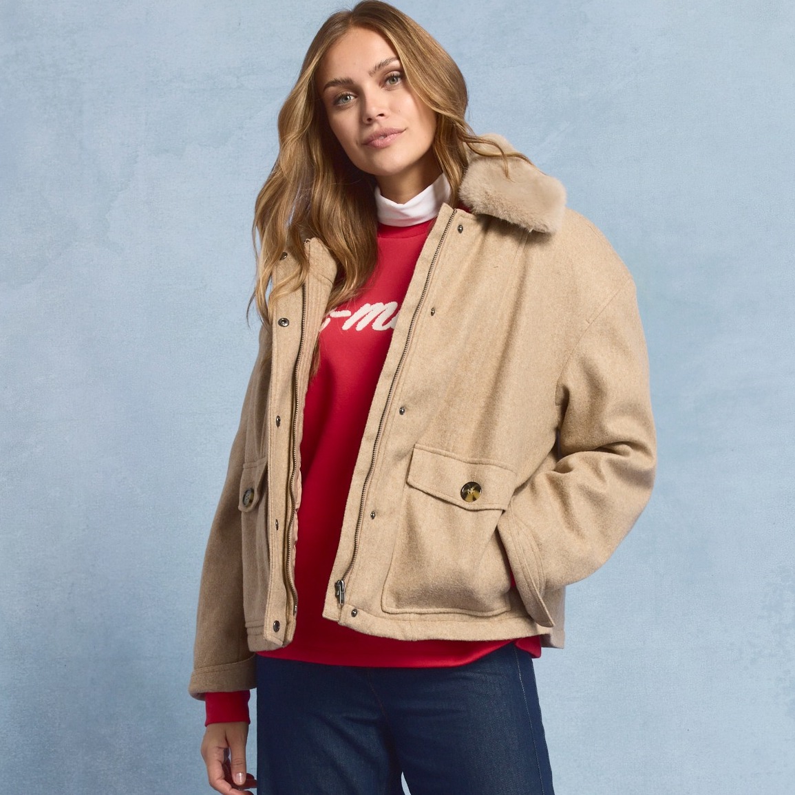 Eine beige Jacke mit Pelzkragen über einem roten Pullover.