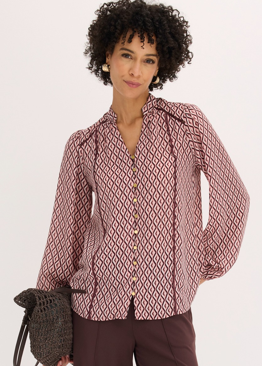 Modische Bluse mit Rautenmuster, langen Ärmeln und kontrastierenden Paspeln, dazu dunkle Hose.