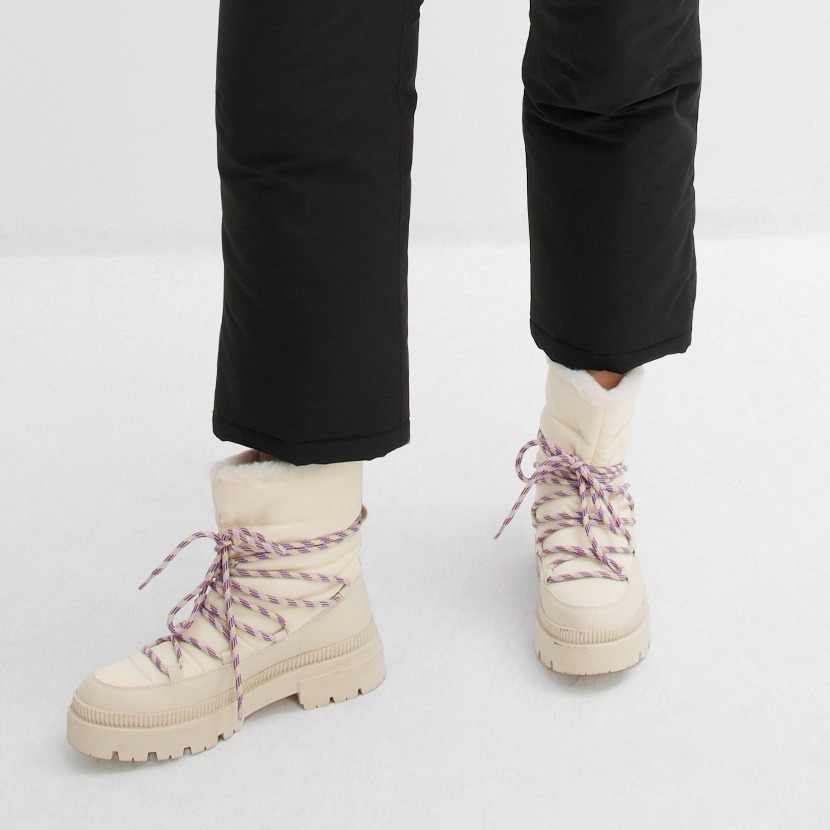 Schwarze Hose trifft auf cremefarbene Stiefel mit rosa Schnürsenkeln. 