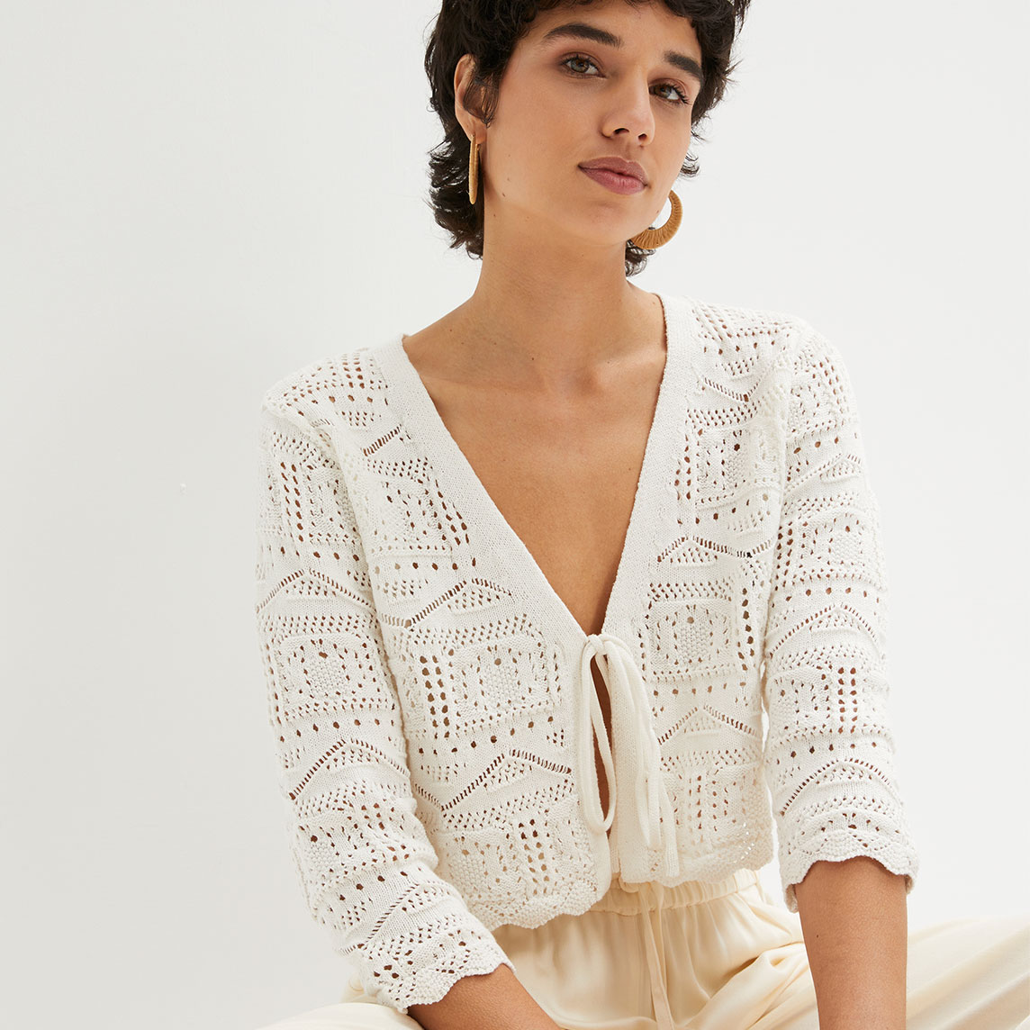 Weiße Häkelstrickjacke mit Bindedetail, kombiniert mit beiger Hose.