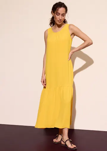 Gelbes ärmelloses Maxikleid kombiniert mit schwarzen Sandalen.