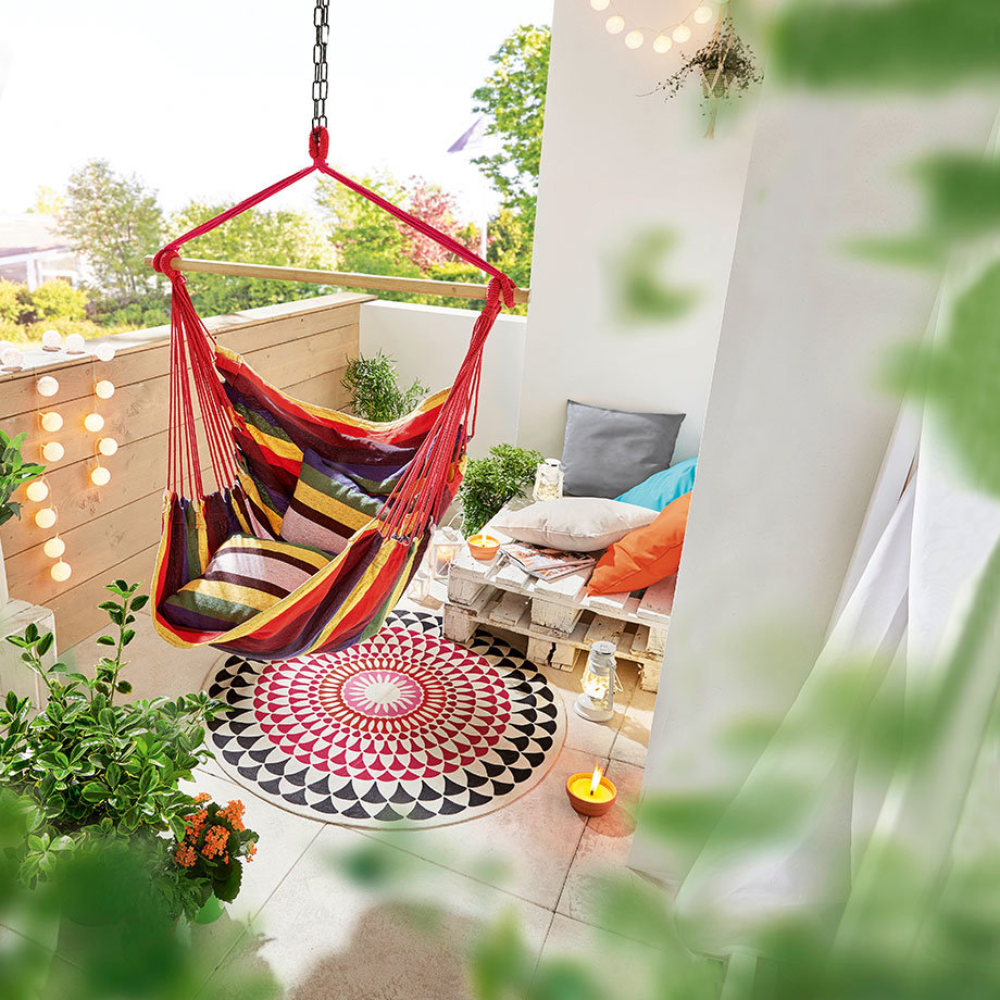 Bunte Hängematte und gemütliche Kissen laden zum Entspannen auf dem sonnigen Balkon ein.