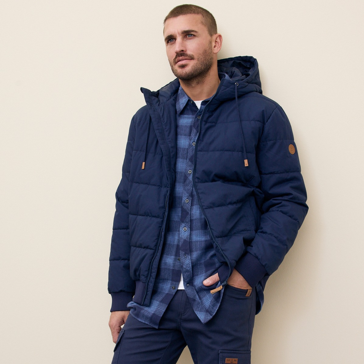 Dunkelblaue Winterjacke mit Kapuze über kariertem Hemd.