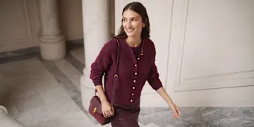 Elegantes burgunderrotes Outfit: Strickjacke mit Goldknöpfen, Oberteil, Hose und passende Tasche.