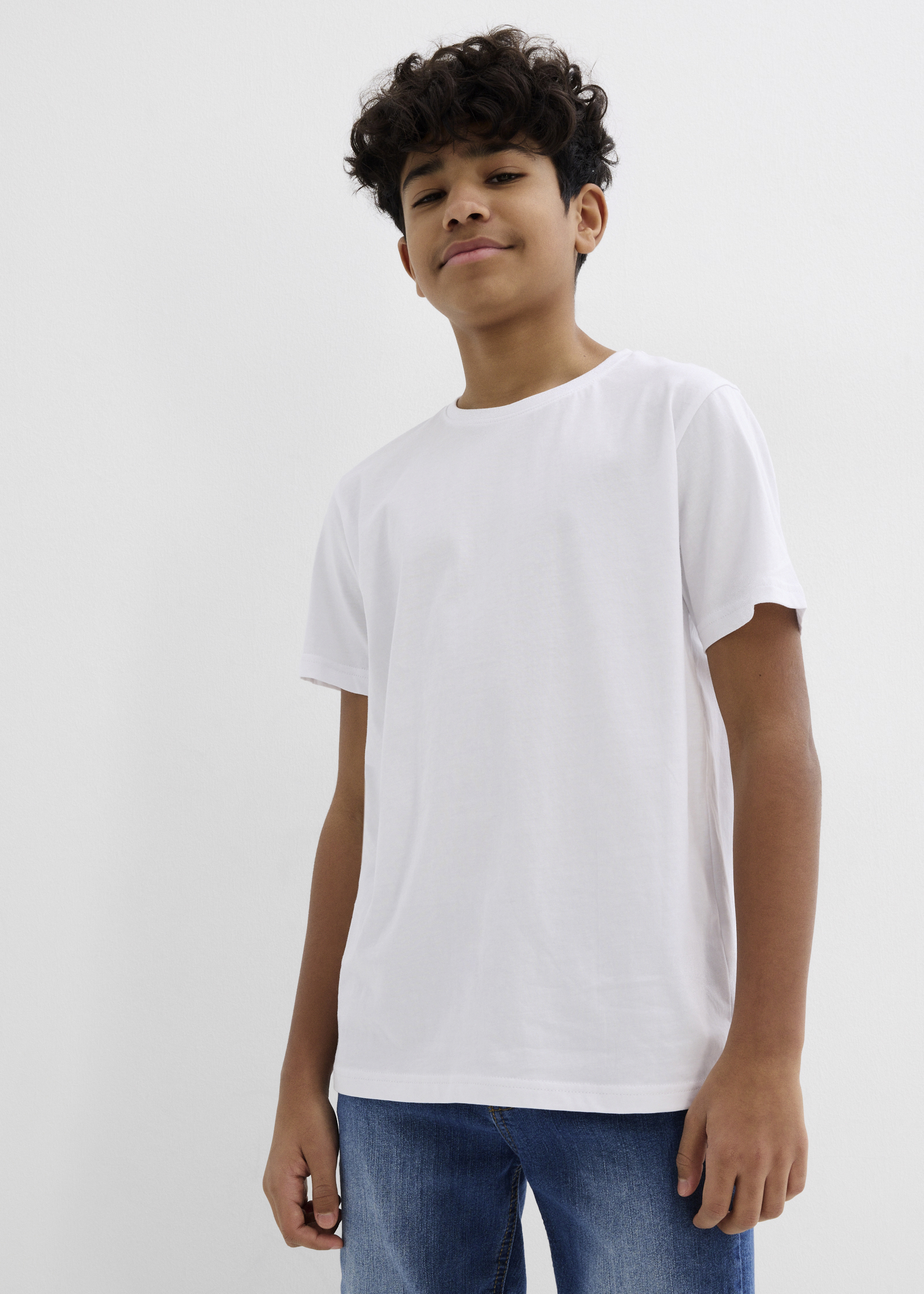 Der Junge trägt ein schlichtes weißes T-Shirt und bequeme blaue Jeans.