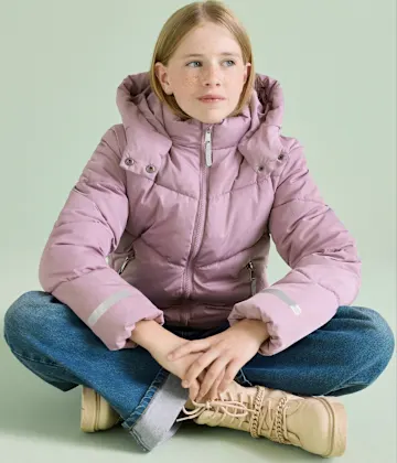 Rosa Steppjacke, blaue Jeans und beigefarbene Stiefel bilden ein warmes Outfit.