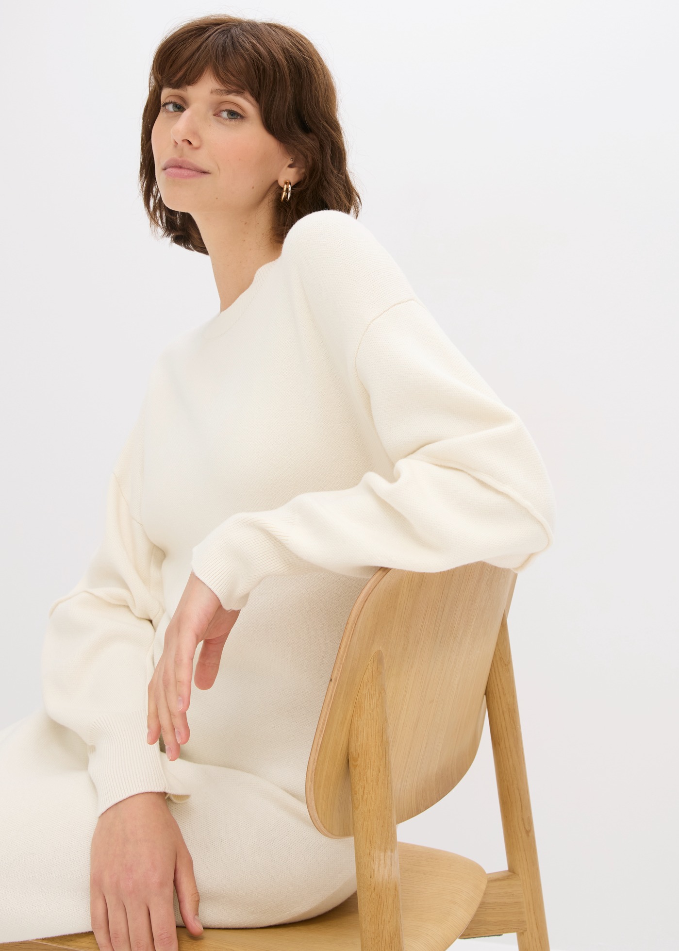 Die Frau trägt ein bequemes, cremefarbenes Strickkleid mit weiten Ärmeln.