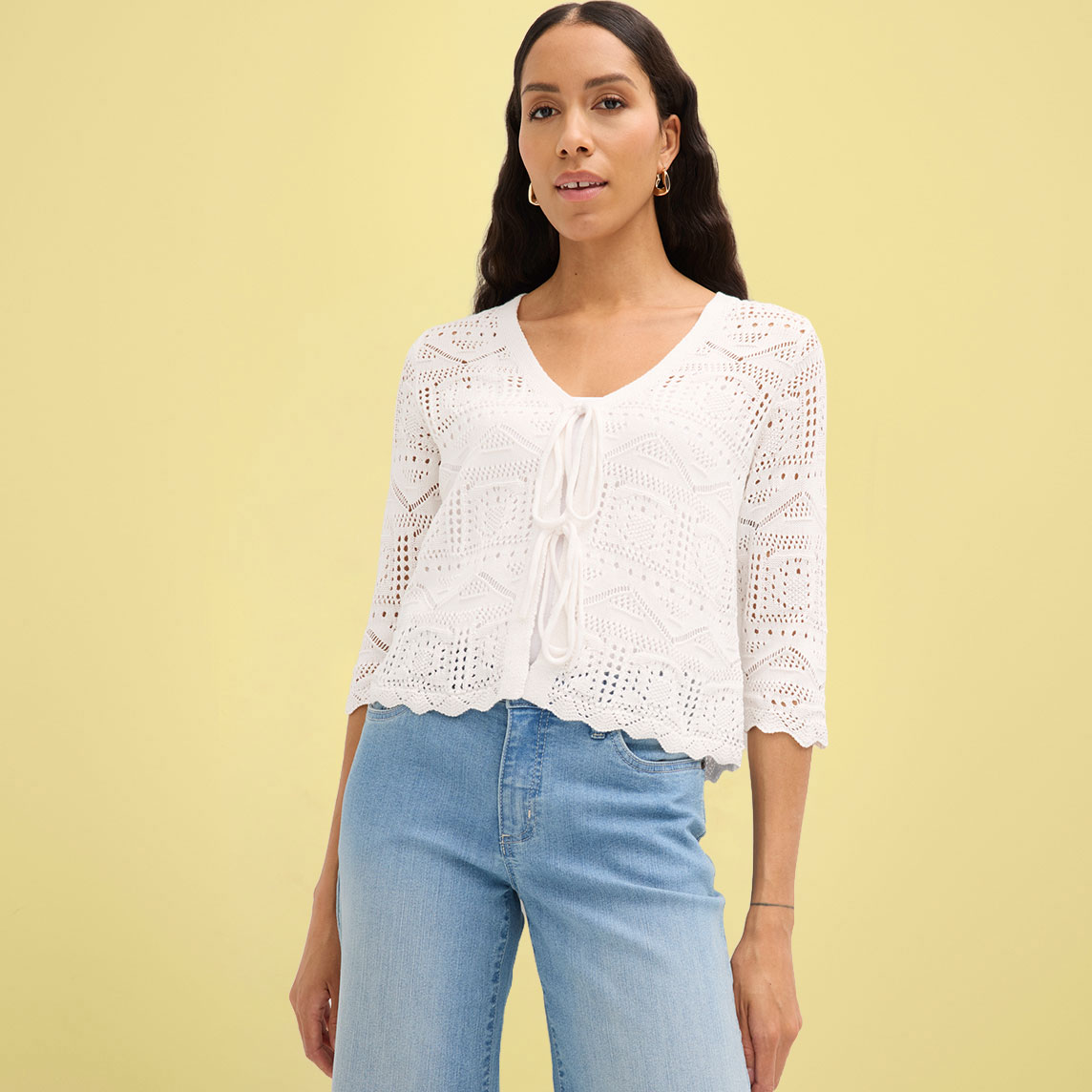 Weiße gehäkelte Strickjacke mit halblangen Ärmeln kombiniert mit blauer Jeans.