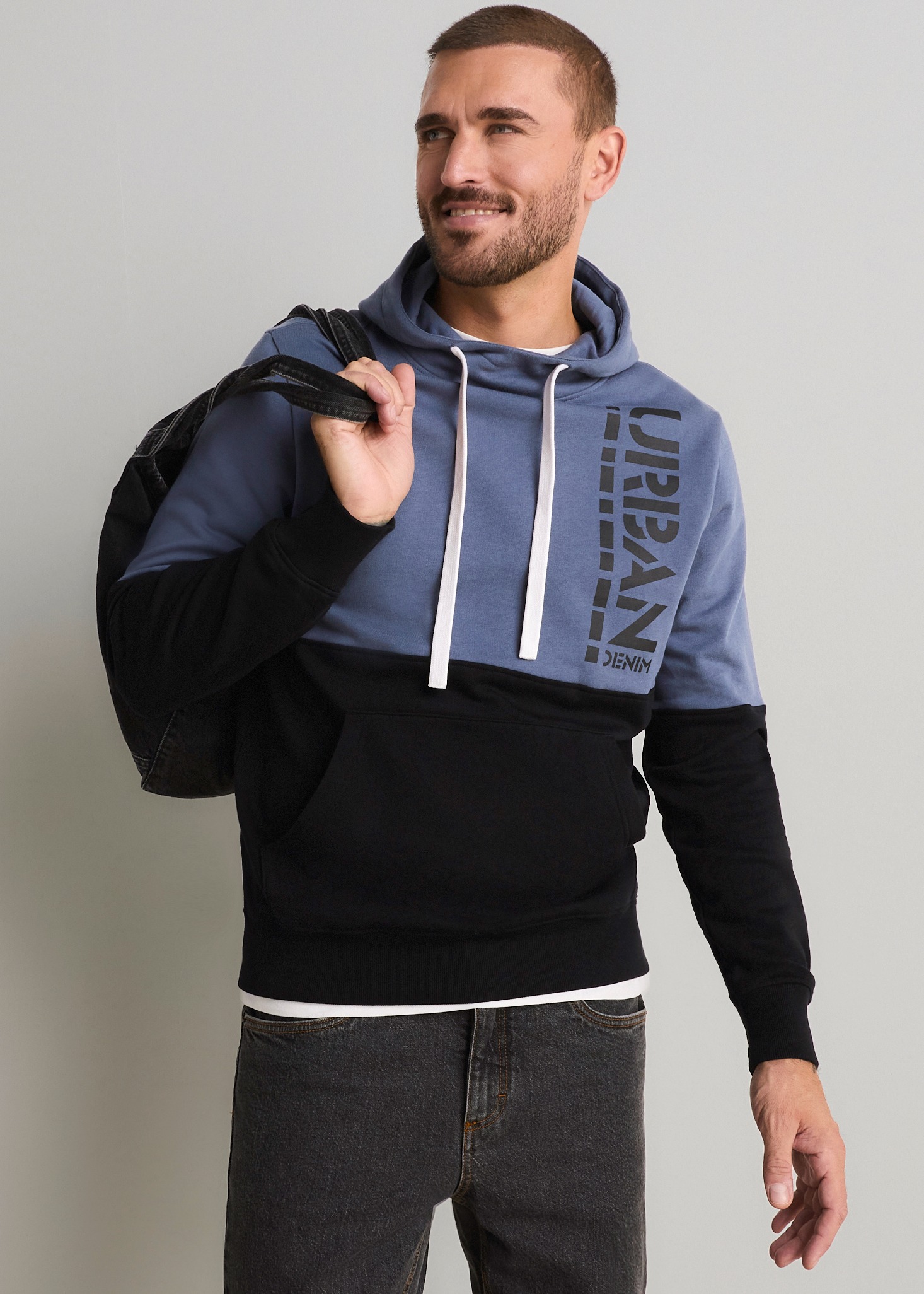 Blauer und schwarzer Hoodie mit URBAN-Print, dunkle Jeans und ein Rucksack.