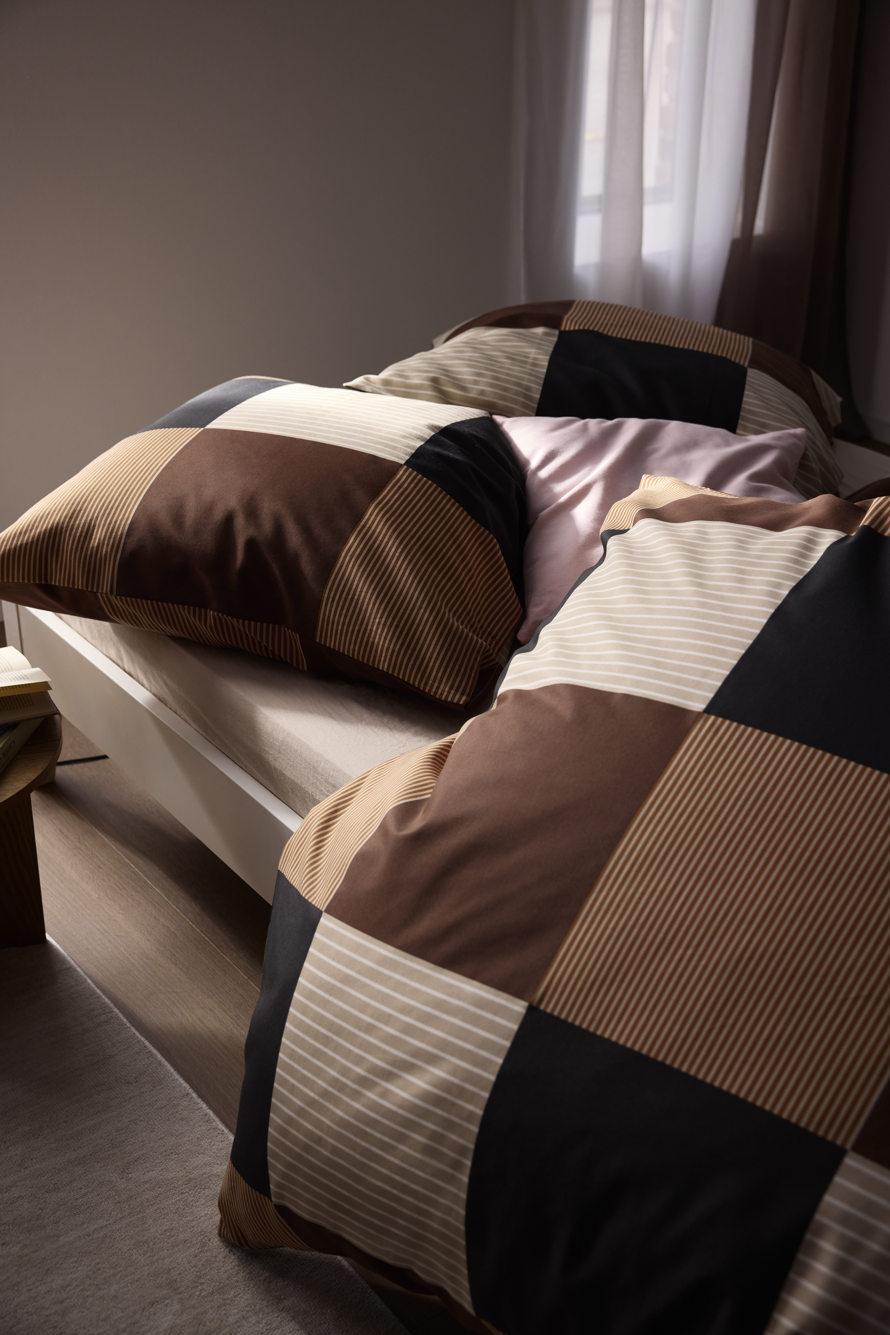Gemütliche Patchwork-Bettwäsche in warmen Braun-, Schwarz- und Beigetönen auf einem Bett.