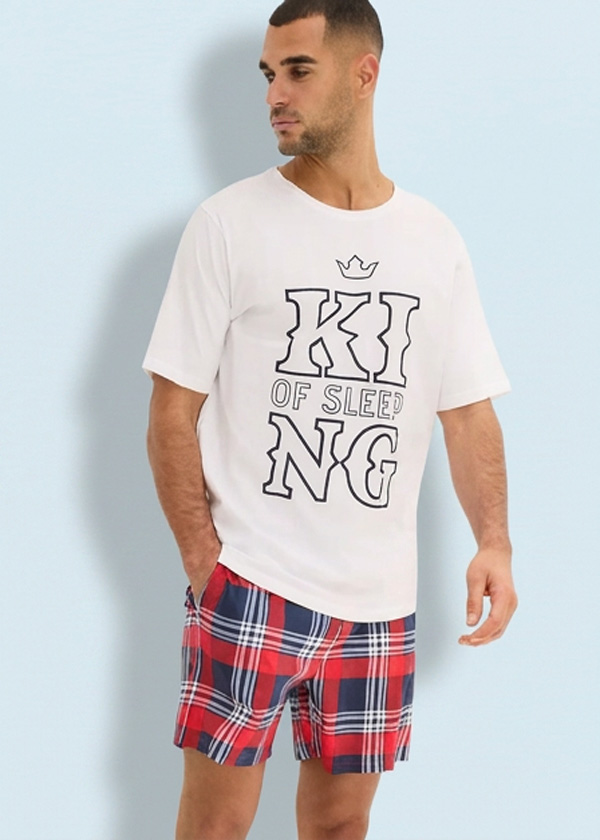 Mann in weißem T-Shirt mit "KING OF SLEEP"-Aufdruck und rot-blau karierten Schlafshorts.