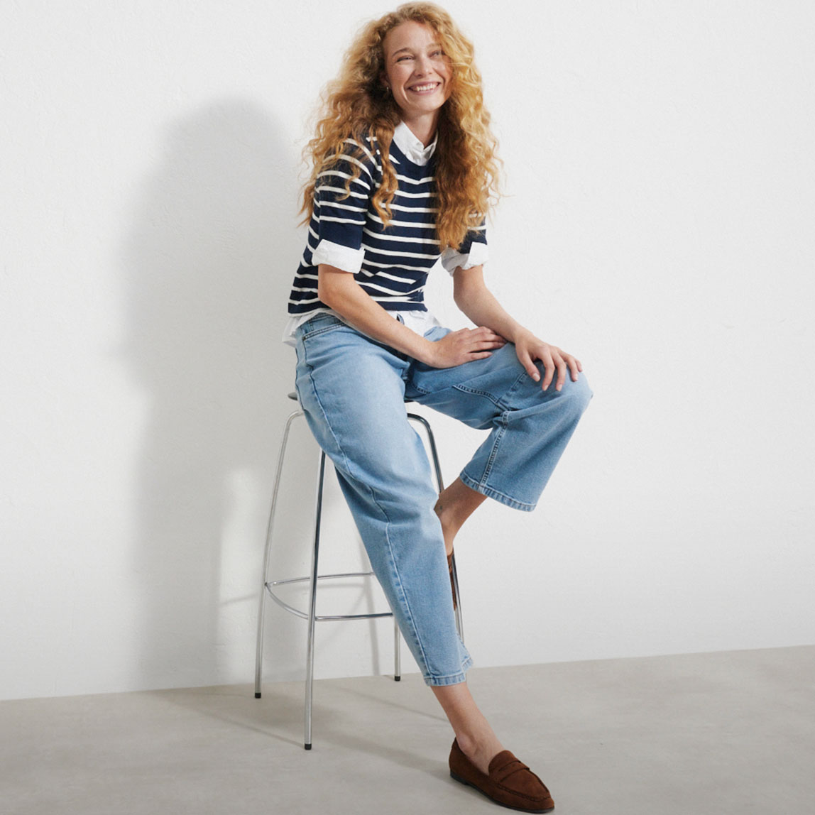 Ringelpullover über Bluse, helle Jeans und braune Loafer.