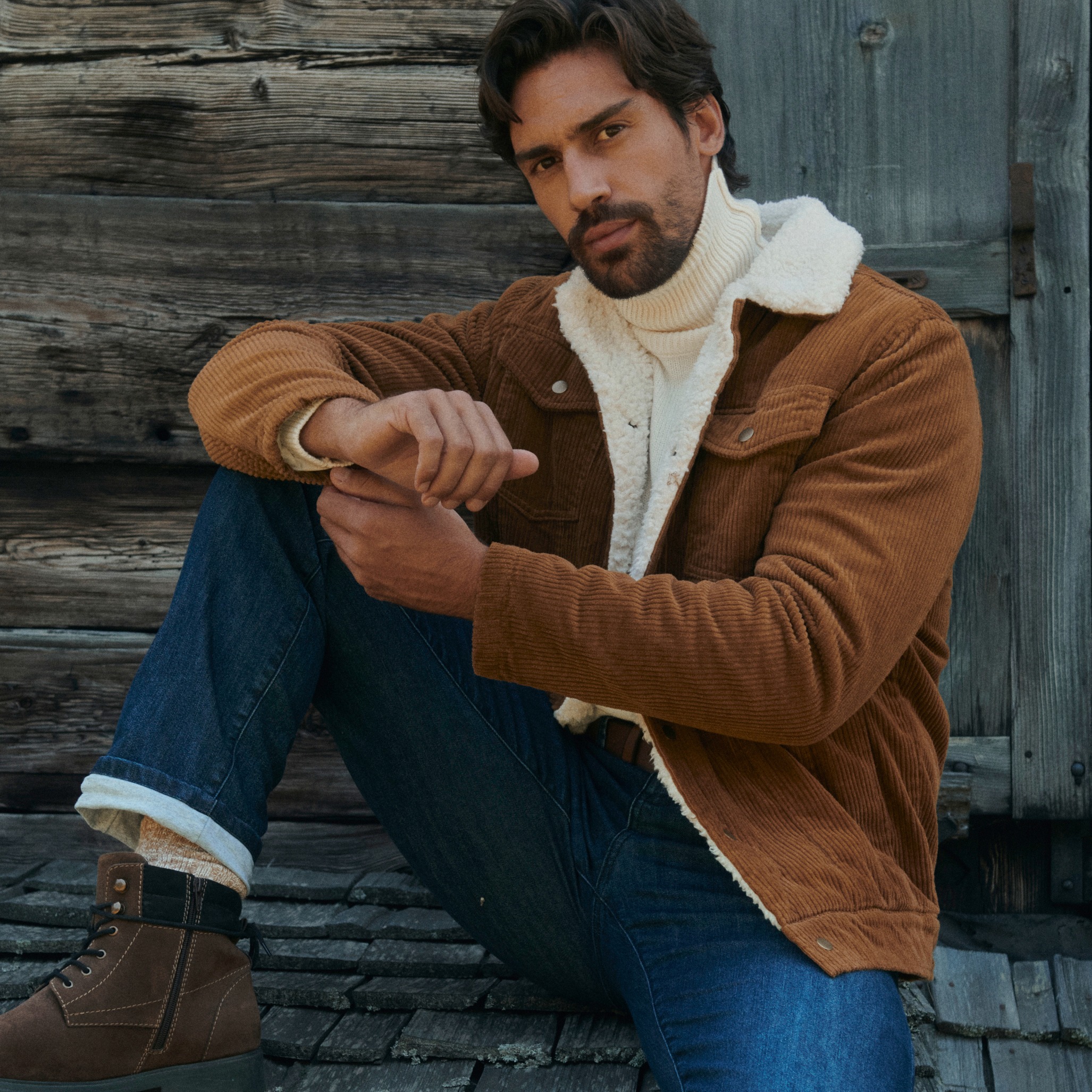 Mann in brauner Cordjacke, weißem Rollkragenpullover, Jeans und warmen Stiefeln.