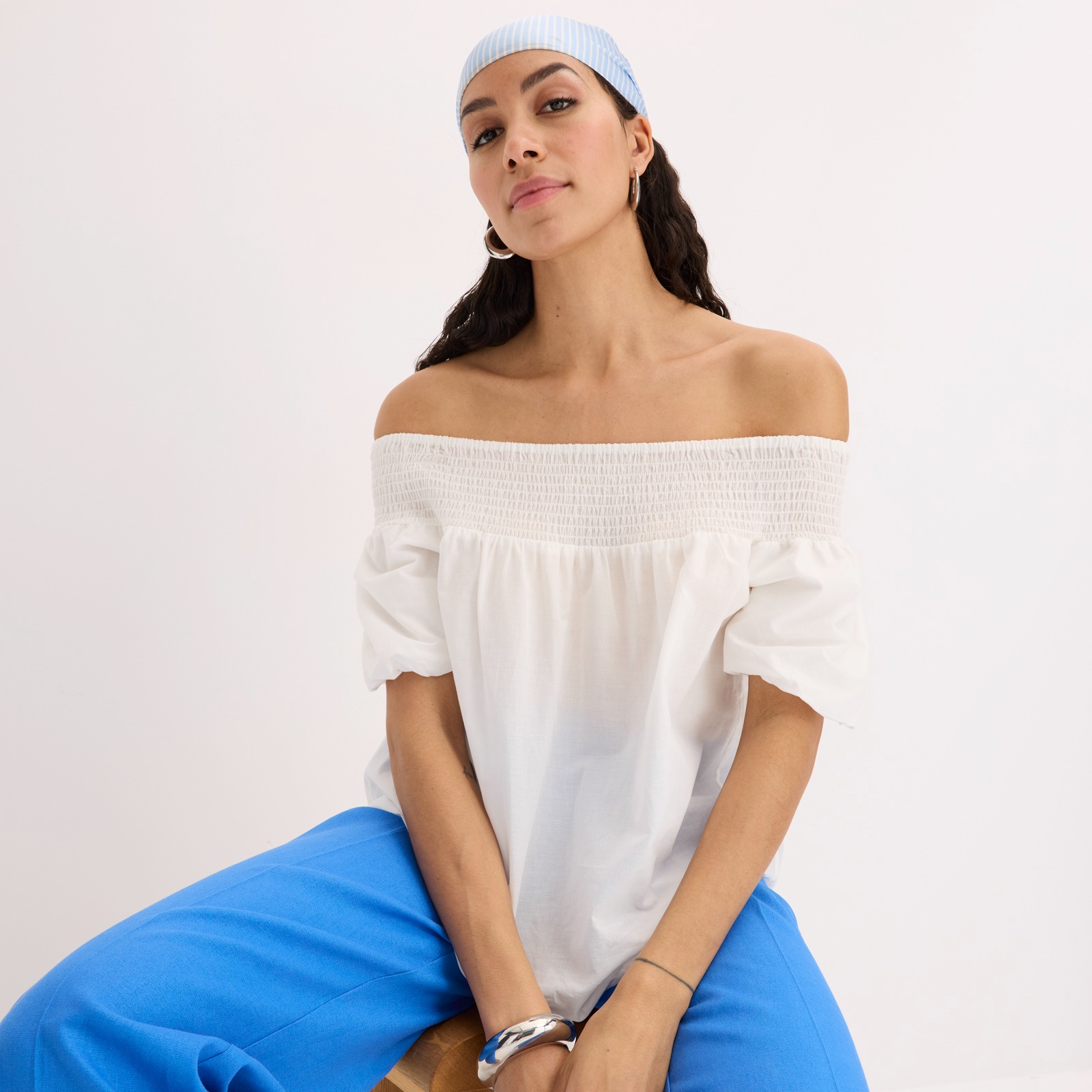 Weiße Schulterfreie Bluse mit kurzen Ärmeln, blaue weite Hose und hellblaues Kopftuch.