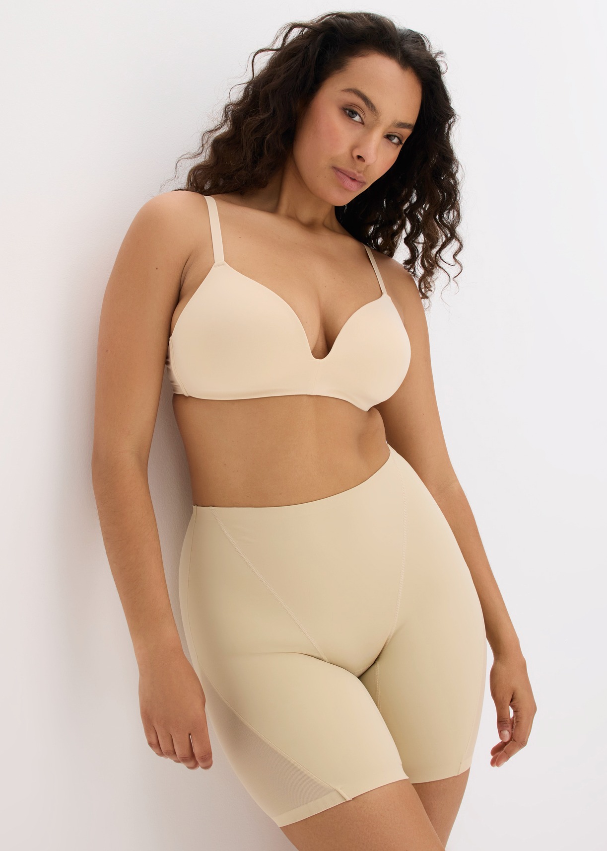 Sie trägt einen beigen BH und passende, formende Shorts in Hautfarbe.