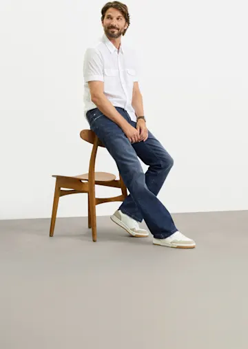 Weißes Kurzarmhemd, dunkle Jeans und weiße Sneaker für einen lässigen Look.