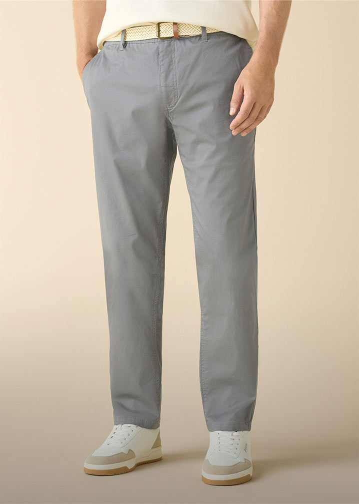 Stilvolle graue Chino, helles Oberteil, geflochtener Gürtel und weiße Sneaker mit beigen Details.