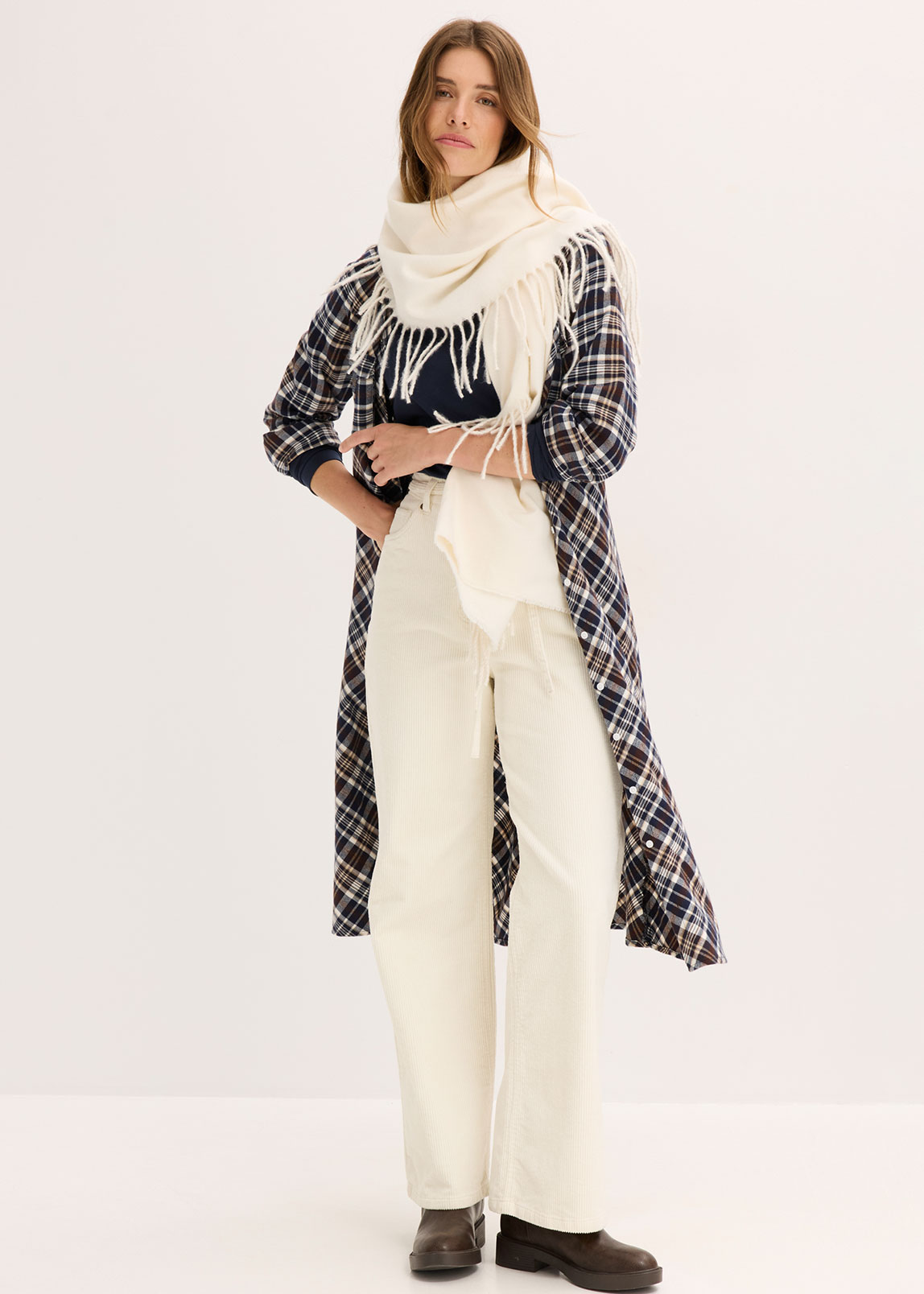 Karierter Mantel über cremefarbenem Outfit mit Rollkragenpullover, weitem Schal und Hose.