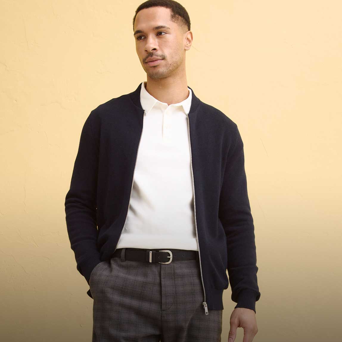 Dunkle Strickjacke über weißem Poloshirt, kombiniert mit grauer Hose.