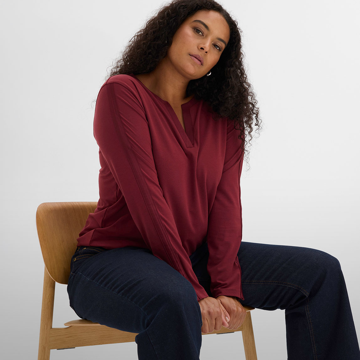 Weinrotes Langarmshirt mit V-Ausschnitt und dunkelblaue Jeans.