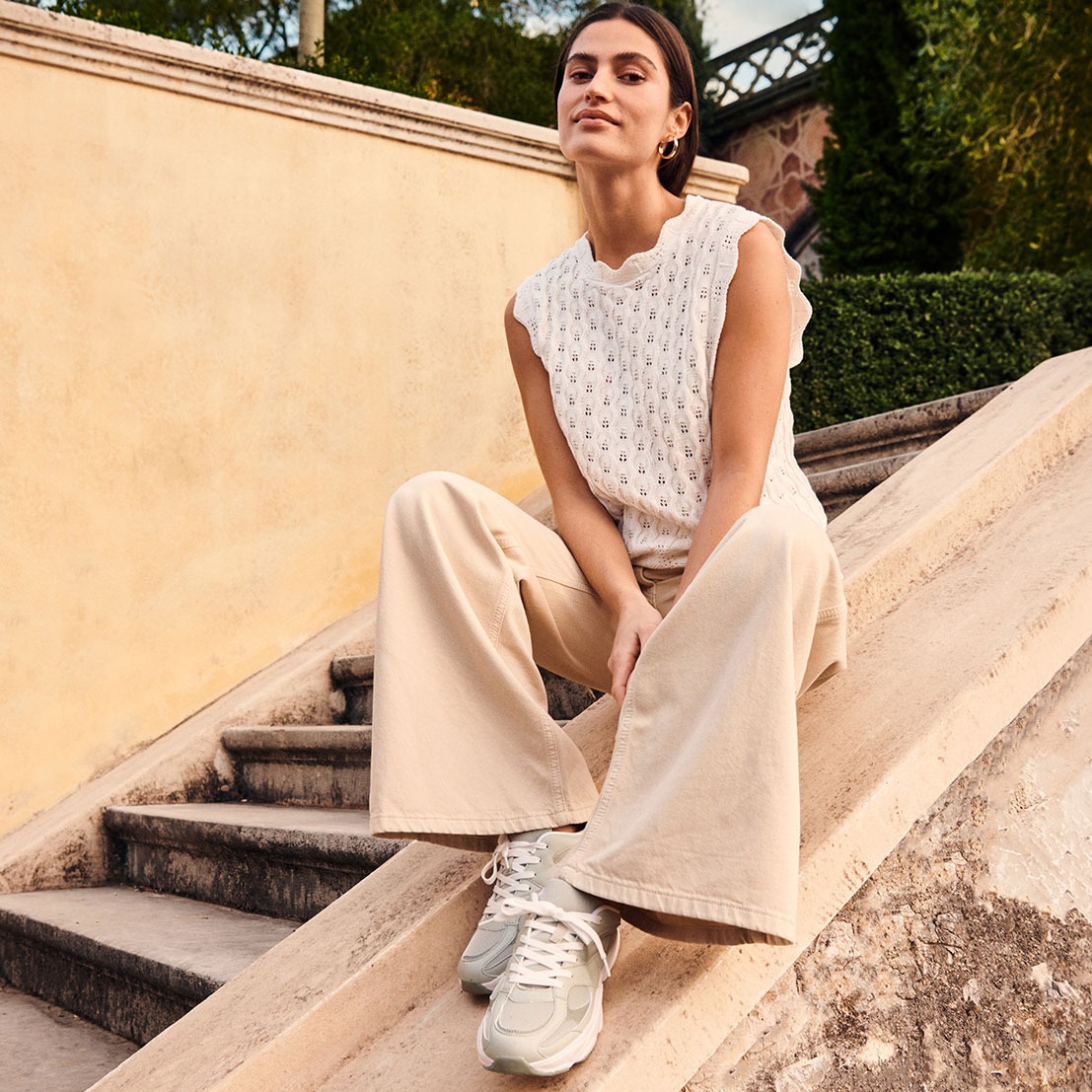 Outfit mit weißem Top, weiter beiger Hosen und bequemen Sneakern.