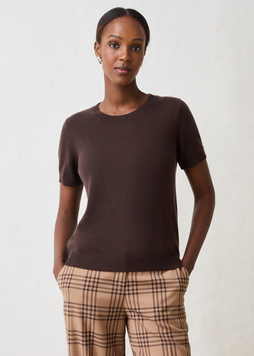 Sie trägt ein elegantes, dunkelbraunes Kurzarm-Oberteil und eine beigefarbene, karierte Hose.