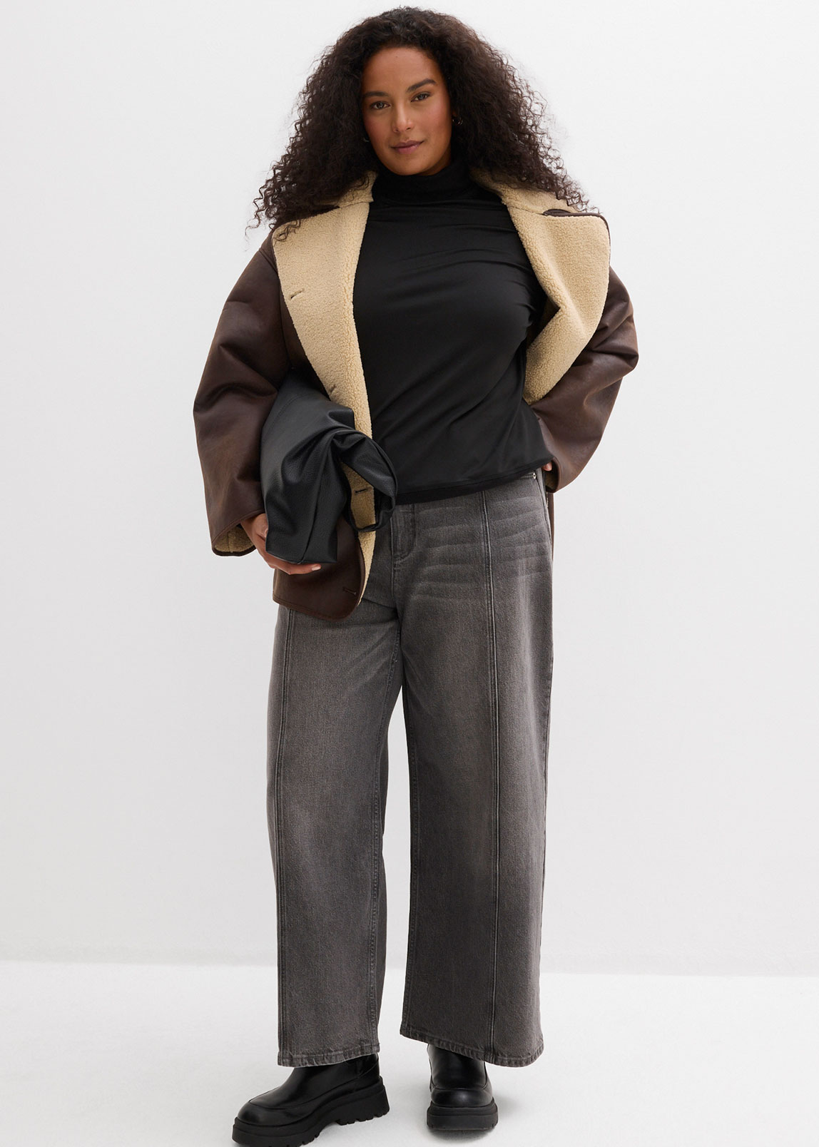 Jacke mit Fellkragen, schwarzer Rollkragenpullover und weite graue Hose.