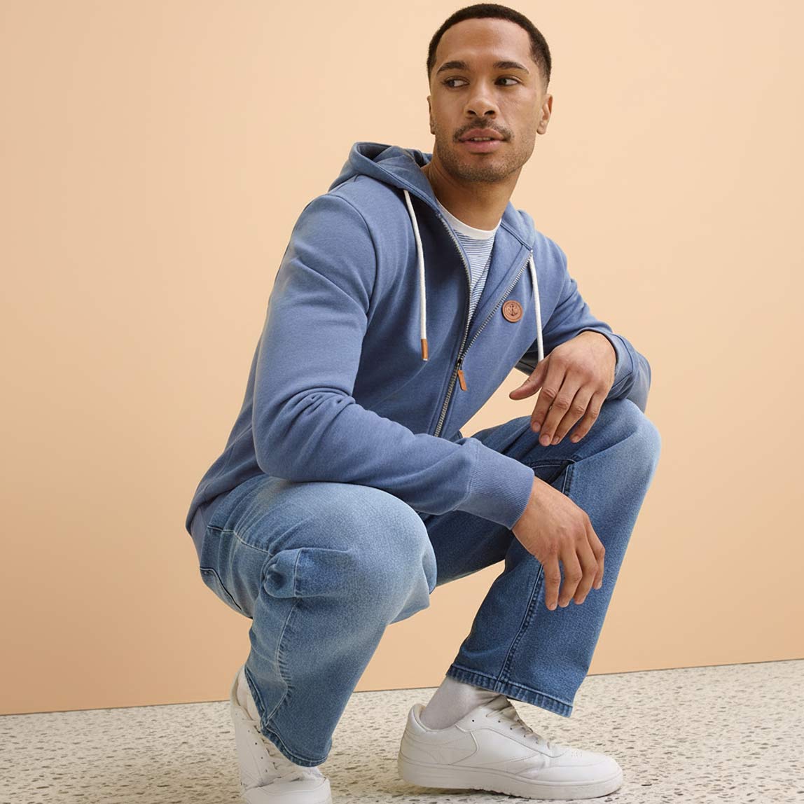 Blauer Kapuzenpullover, verwaschene Jeans und weißen Sneakers. 