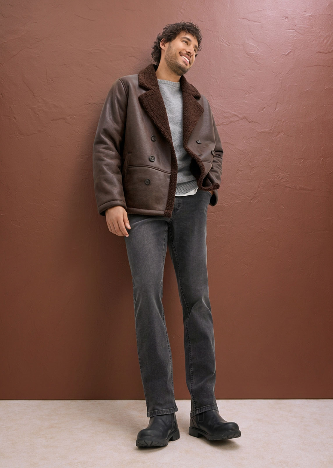 Lässiger Stil: braune Lammfelljacke, grauer Pullover, dunkle Jeans und robuste schwarze Stiefel.