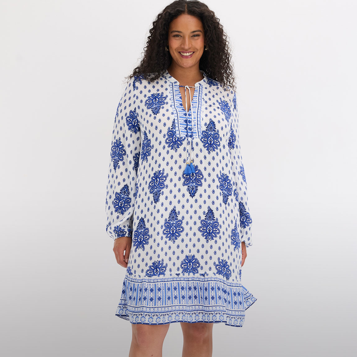 Weiß-blaues Tunikakleid mit Ethno-Muster, Bindebändern und langen Ärmeln.