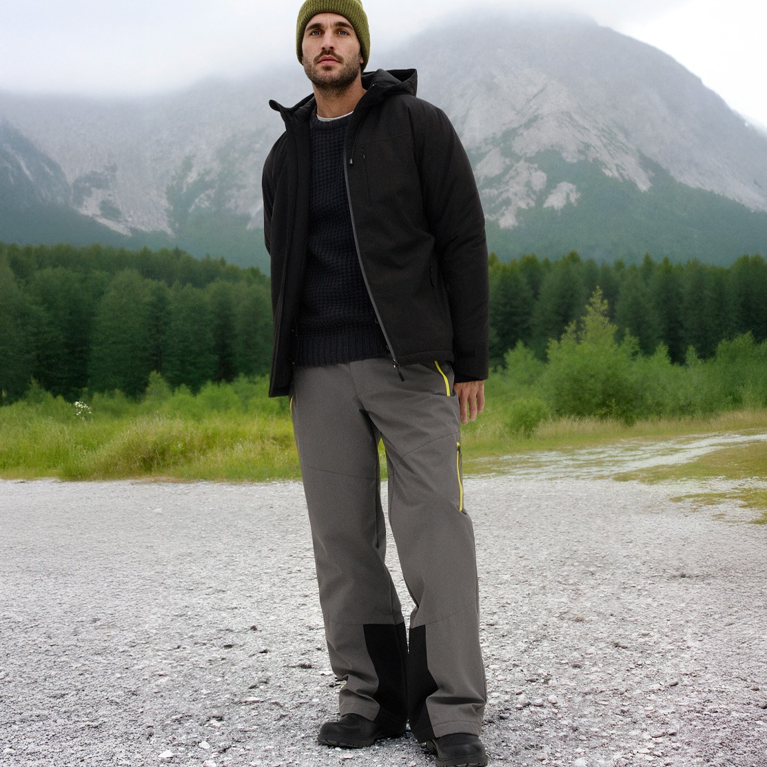 Dunkle Winterjacke, graue Hose und grüne Mütze.